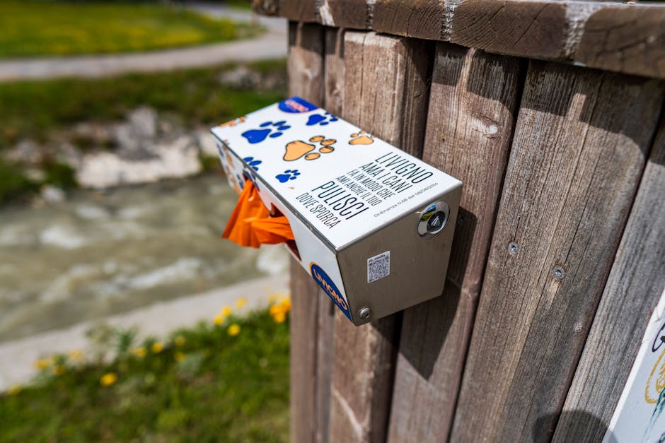 Dog waste bag dispenser mounted on wooden fence in scenic Livigno, Italy.